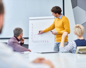 Portrait of young businessman standing at whiteboard drawing graph during marketing meeting in board room